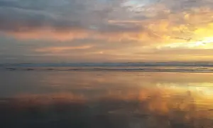 Piękny wschód słońca rysunek na niebie, odbijający się w mokrym piasku plaży.
