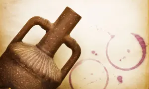 Brązowa amfora z dwoma uchwytami i ozdobnym brzuścem, obok plamy po winie. To jest amfora, starożytny dzban.