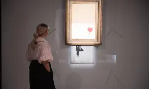 Kobieta ogląda słynne dzieło Banksy'ego, które uległo samozniszczeniu. Obraz z czerwonym balonem w kształcie serca jest częściowo zniszczony.
