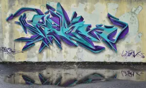 Wielobarwne, przestrzenne graffiti w odcieniach turkusu i fioletu zdobi ścianę. To przykład sztuki ulicznej, która często jest formą wyrazu artystycznego.