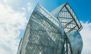 Szklane żagle Fundacji Louis Vuitton odbijają błękitne niebo i chmury.