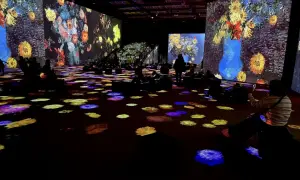 Wystawa Van Gogh: widzowie zanurzeni w projekcjach słoneczników i innych dzieł, siedzą na podłodze oświetlonej kolorowymi plamami.