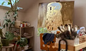 Artystyczna pracownia z reprodukcją "Pocałunku" Klimta, roślinami i pędzlami.