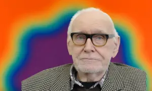 Starszy mężczyzna w okularach na tle tęczowego obrazu, być może najdroższy malarz współczesny.