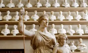 W muzeum pełnym białych popiersi, które wyglądają jak repliki antycznych rzeźb, na pierwszym planie widać dwie figury.