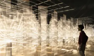 Mężczyzna podziwia trójwymiarowe dzieło sztuki z białych, półprzezroczystych tkanin, tworzących świetlistą instalację.