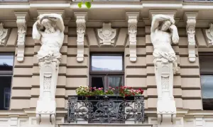 Dwie rzeźby atlantesów podtrzymują balkon w stylu secesyjnym. Kwiaty dodają koloru tej architekturze.