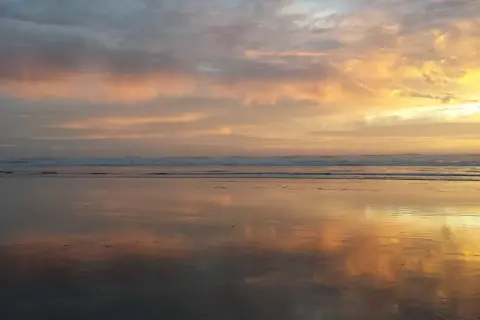 Piękny wschód słońca rysunek na niebie, odbijający się w mokrym piasku plaży.
