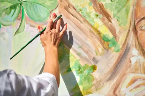 Artystka maluje obraz, który może być przeznaczony do sprzedaży obrazów bez działalności gospodarczej. Widać jej dłoń z pędzlem i fragment twarzy.