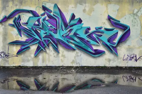 Wielobarwne, przestrzenne graffiti w odcieniach turkusu i fioletu zdobi ścianę. To przykład sztuki ulicznej, która często jest formą wyrazu artystycznego.