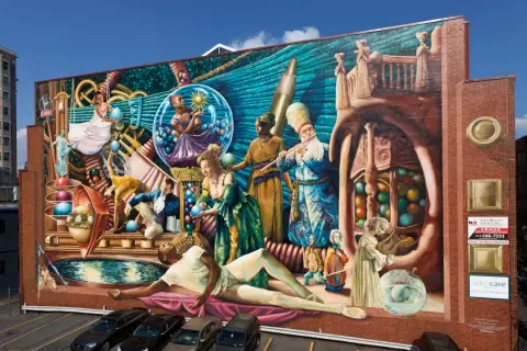 Wielobarwny mural przedstawia surrealistyczną scenę z ludźmi w historycznych strojach, kulami i instrumentami.