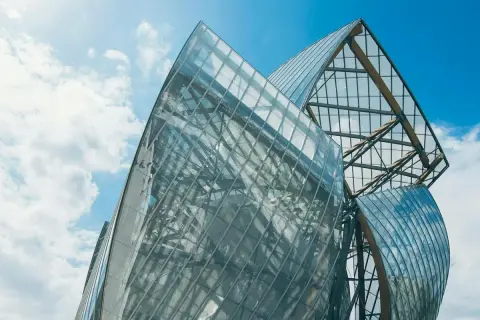 Szklane żagle Fundacji Louis Vuitton odbijają błękitne niebo i chmury.