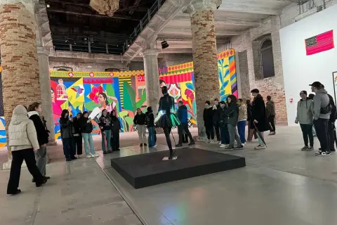 Grupa zwiedzających ogląda barwne instalacje w galerii. To właśnie jest biennale – świat sztuki w pigułce.