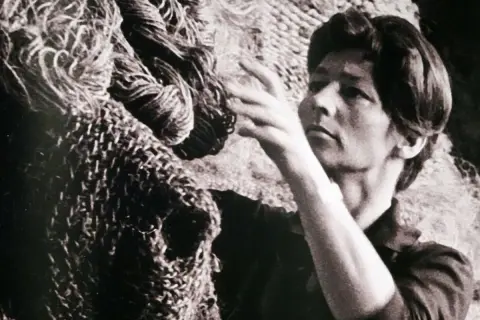 Magdalena Abakanowicz z dłońmi wśród swoich monumentalnych, plecionych dzieł, abakanów.