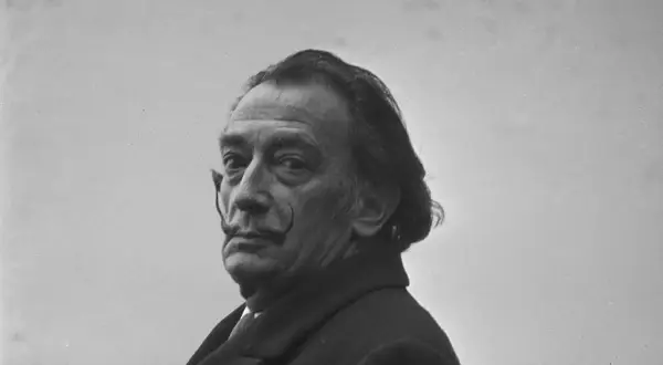 Salvador Dalí, z charakterystycznym wąsem i spojrzeniem, w płaszczu. Ciekawe fakty o jego życiu i sztuce.