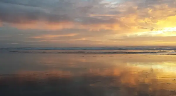 Piękny wschód słońca rysunek na niebie, odbijający się w mokrym piasku plaży.