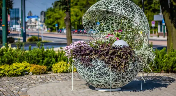Ozdobna kula z kwiatami, przykład instalacji artystycznej. Wplecione w ażurową konstrukcję rośliny tworzą efektowną kompozycję.