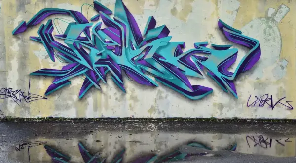 Wielobarwne, przestrzenne graffiti w odcieniach turkusu i fioletu zdobi ścianę. To przykład sztuki ulicznej, która często jest formą wyrazu artystycznego.
