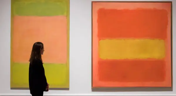 Kobieta podziwia dwa abstrakcyjne obrazy Marka Rothko. Jeden z nich, z dominującymi kolorami zieleni i brzoskwini, jest uznawany za najdroższy obraz tego artysty.