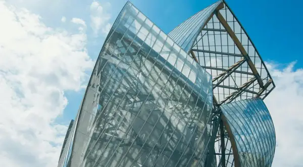Szklane żagle Fundacji Louis Vuitton odbijają błękitne niebo i chmury.