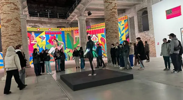 Grupa zwiedzających ogląda barwne instalacje w galerii. To właśnie jest biennale – świat sztuki w pigułce.