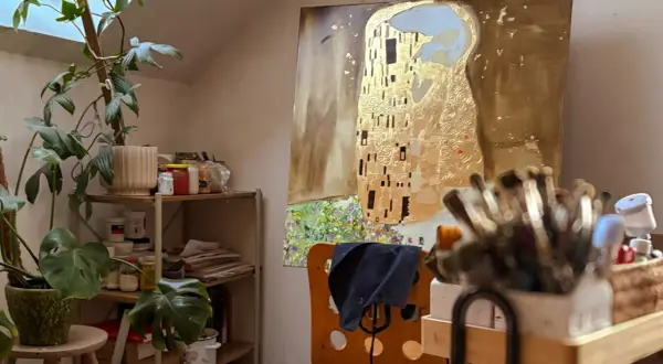 Artystyczna pracownia z reprodukcją "Pocałunku" Klimta, roślinami i pędzlami.