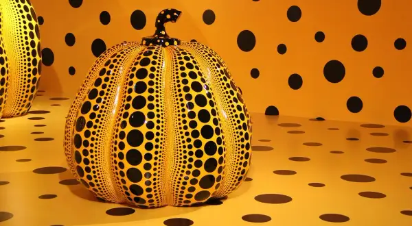 Żółta dynia w czarne kropki, charakterystyczna dla yayoi kusama obrazy, na tle ściany i podłogi w tym samym wzorze.