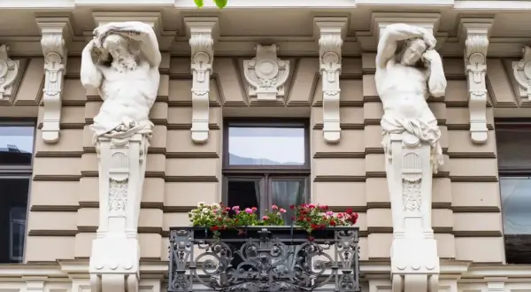 Dwie rzeźby atlantesów podtrzymują balkon w stylu secesyjnym. Kwiaty dodają koloru tej architekturze.