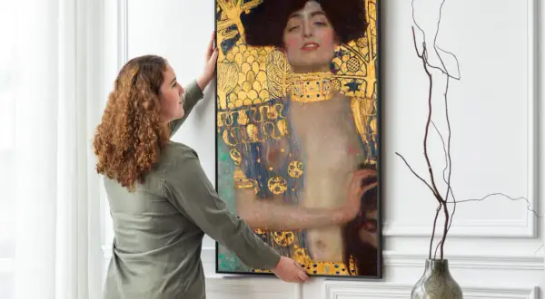 Kobieta wiesza obraz "Judyta z głową Holofernesa" Klimta. Złote zdobienia i mroczna atmosfera dzieła przyciągają wzrok.