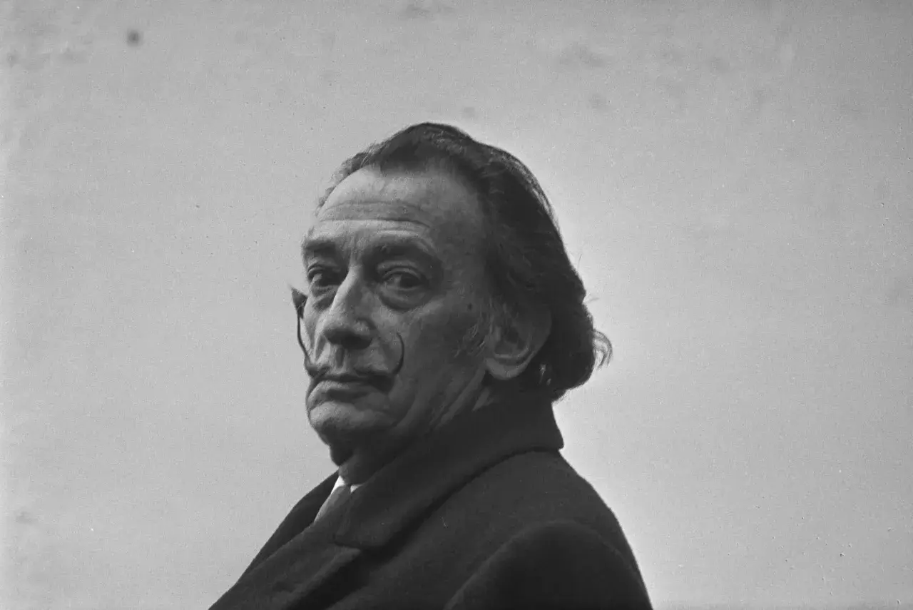 Salvador Dalí, z charakterystycznym wąsem i spojrzeniem, w płaszczu. Ciekawe fakty o jego życiu i sztuce.