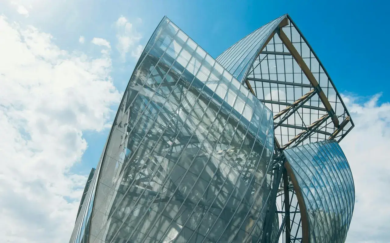 Szklane żagle Fundacji Louis Vuitton odbijają błękitne niebo i chmury.