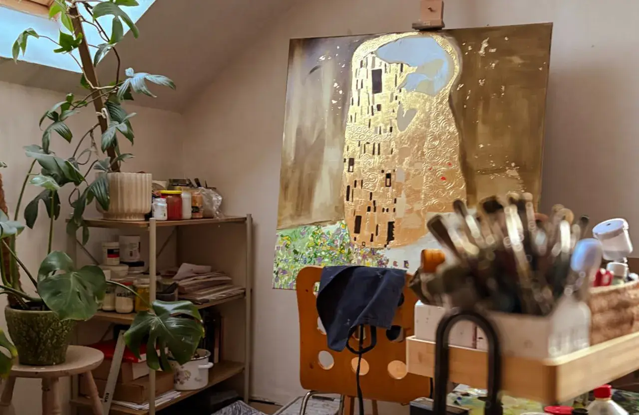 Artystyczna pracownia z reprodukcją "Pocałunku" Klimta, roślinami i pędzlami.