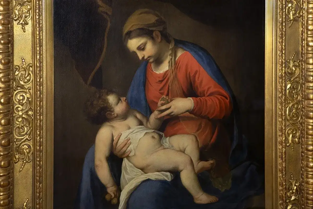 Obraz przedstawia czułą scenę: Madonna z Dzieciątkiem w złotych ramach. Matka z miłością spogląda na synka, który trzyma w rączce owoc.