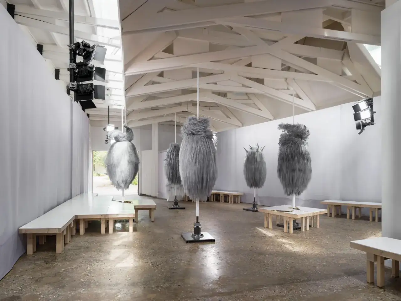 Instalacja artystyczna z szarymi, futrzanymi formami wiszącymi w przestrzeni wystawienniczej. Czy to część wystawy biennale?