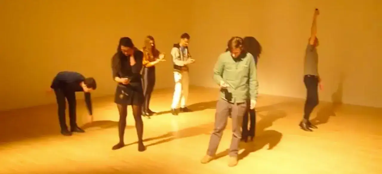Grupa ludzi wpatrzona w telefony, zastanawiająca się, co to jest performance. Jeden z nich podnosi rękę w geście pytania.