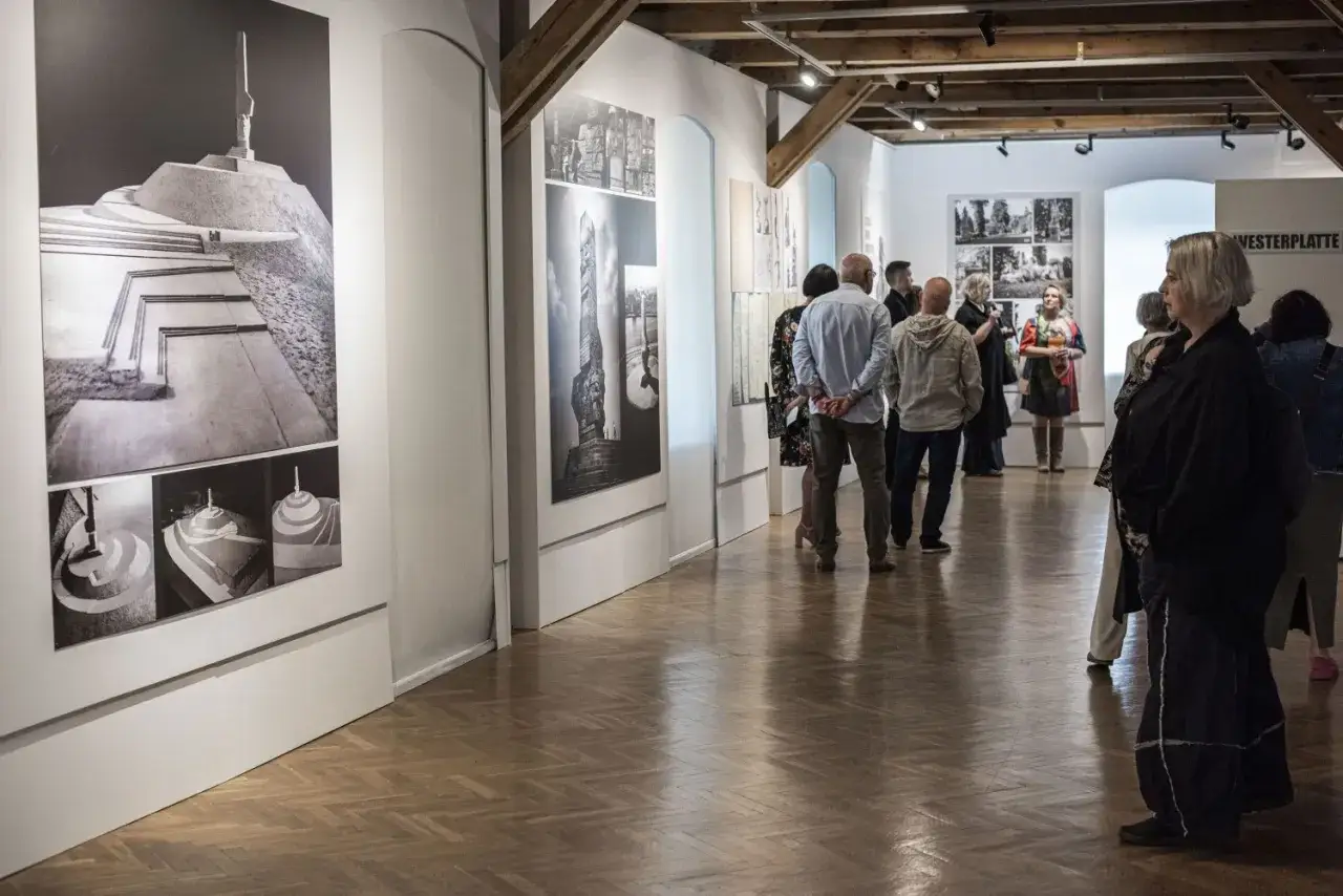 Ludzie oglądają czarno-białe fotografie na ścianach galerii sztuki.