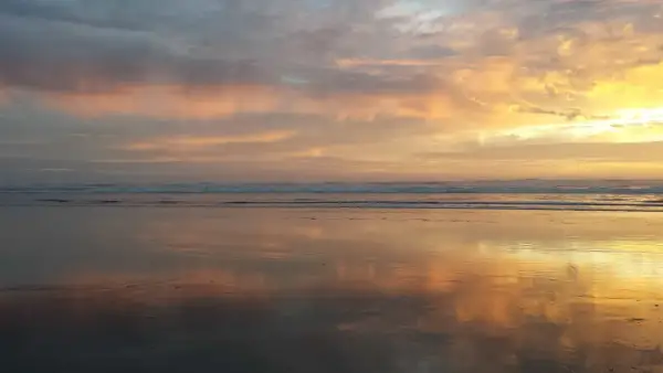 Piękny wschód słońca rysunek na niebie, odbijający się w mokrym piasku plaży.