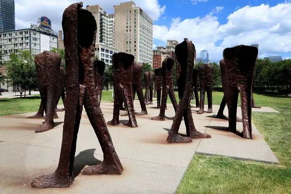 Rzeźby Magdaleny Abakanowicz, grupa bezgłowych postaci w brązie, stoi na placu w mieście.