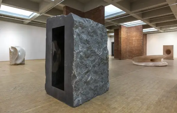 Kamienna rzeźba z czarnym wnętrzem, część wystawy Anish Kapoor w Orońsku. W tle inne dzieła sztuki.