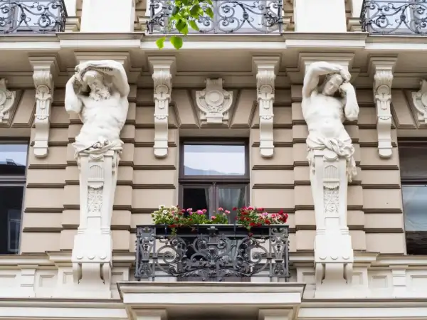 Dwie rzeźby atlantesów podtrzymują balkon w stylu secesyjnym. Kwiaty dodają koloru tej architekturze.
