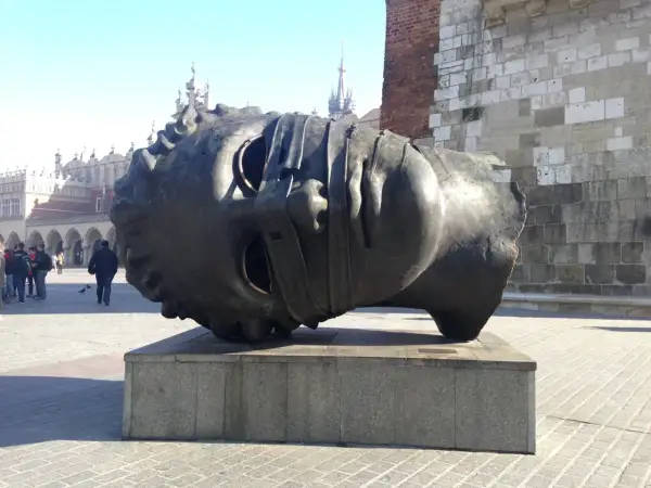 Gigantyczna, metalowa głowa leży na cokole. To intrygująca rzeźba, która przyciąga wzrok przechodniów na rynku.