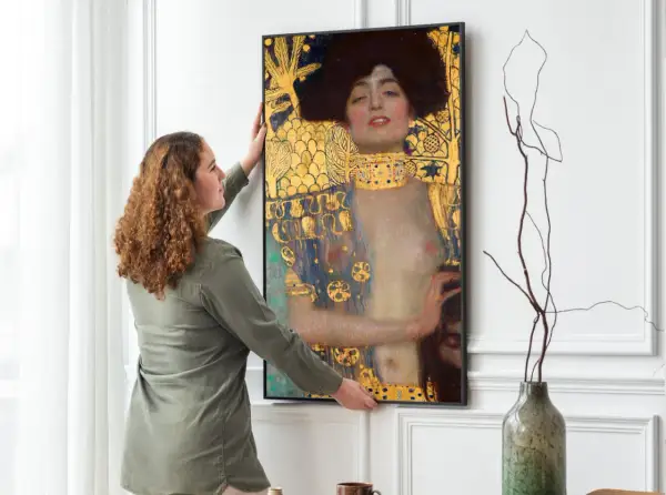Kobieta wiesza obraz "Judyta z głową Holofernesa" Klimta. Złote zdobienia i mroczna atmosfera dzieła przyciągają wzrok.